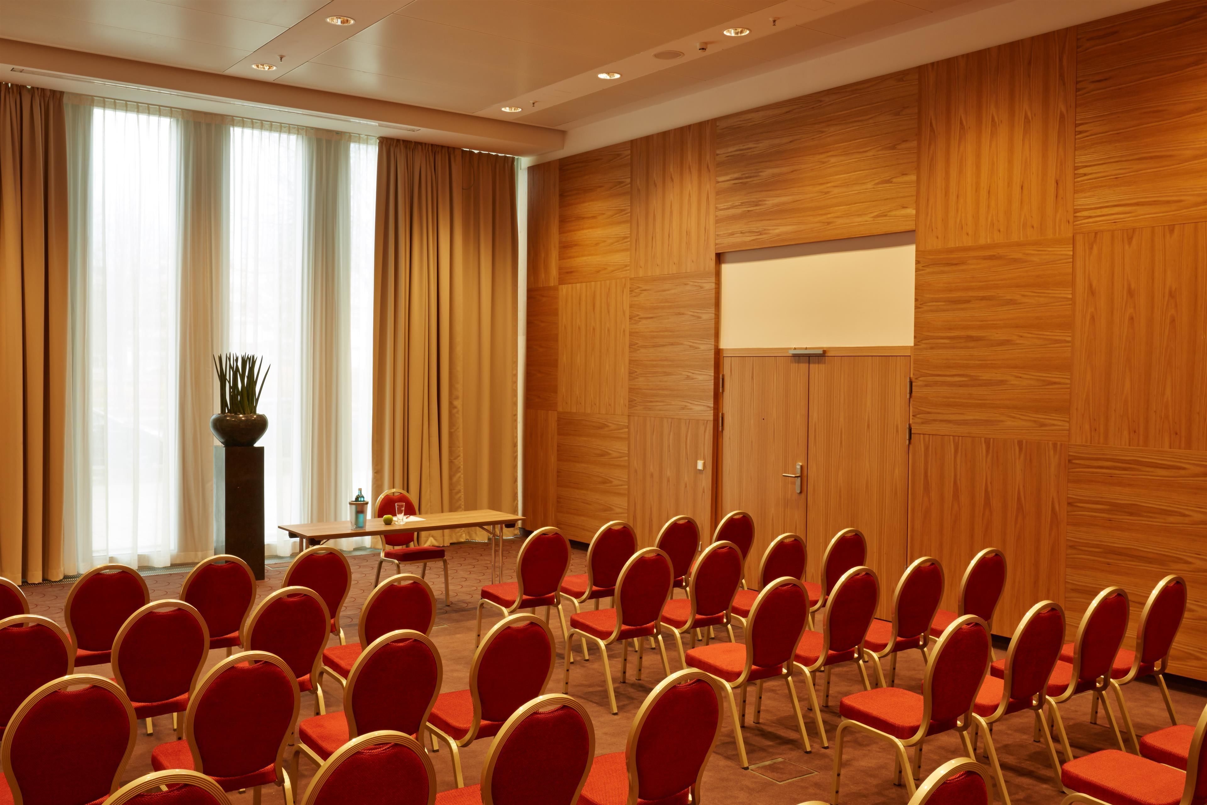 A conference room with rows of red chairs, a projector screen, and a large potted plant.