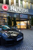 Edifício do H4 Hotel com um carro preto na frente.