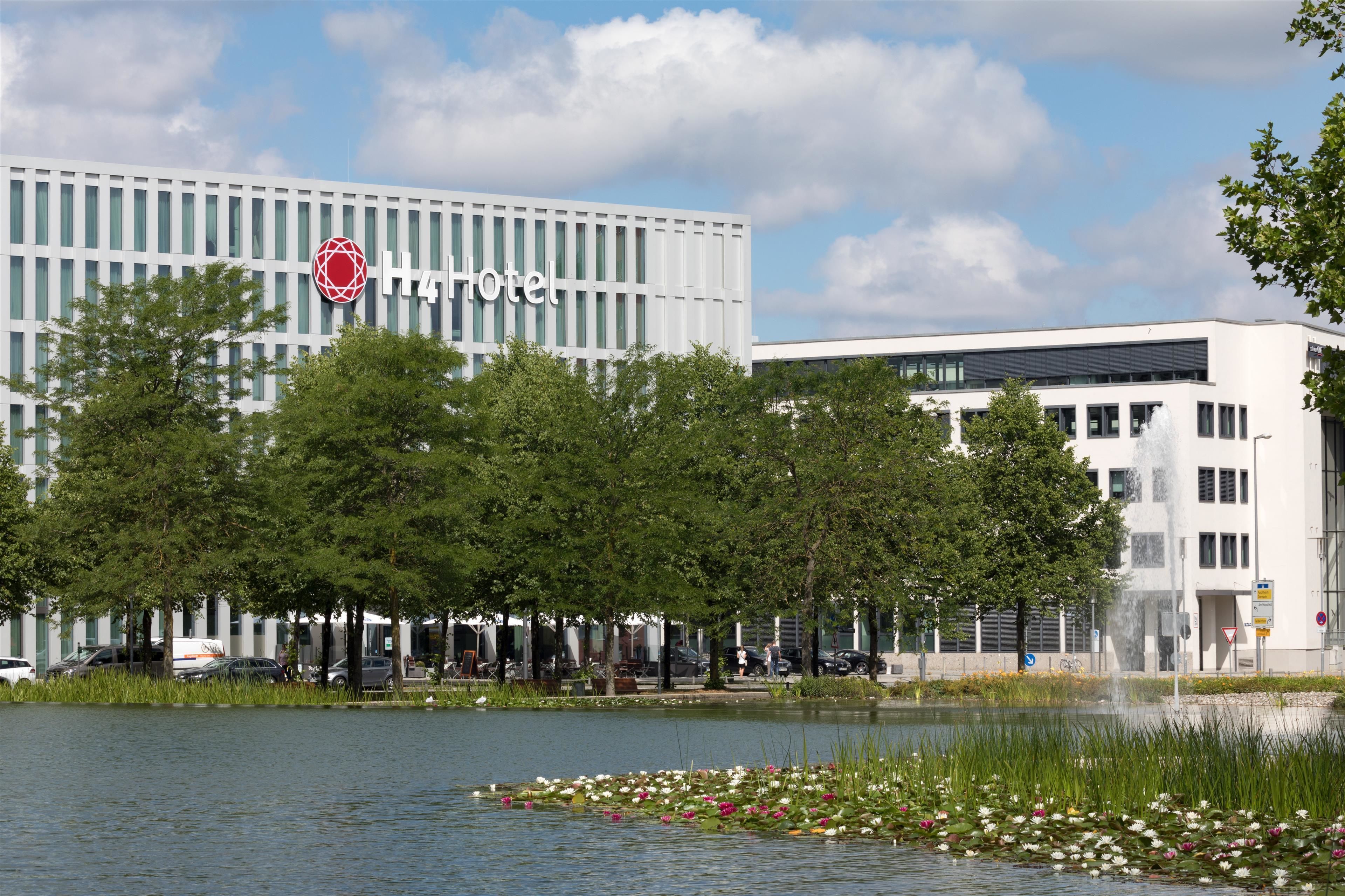A modern hotel with a prominent logo, a water feature, and a well-maintained garden.