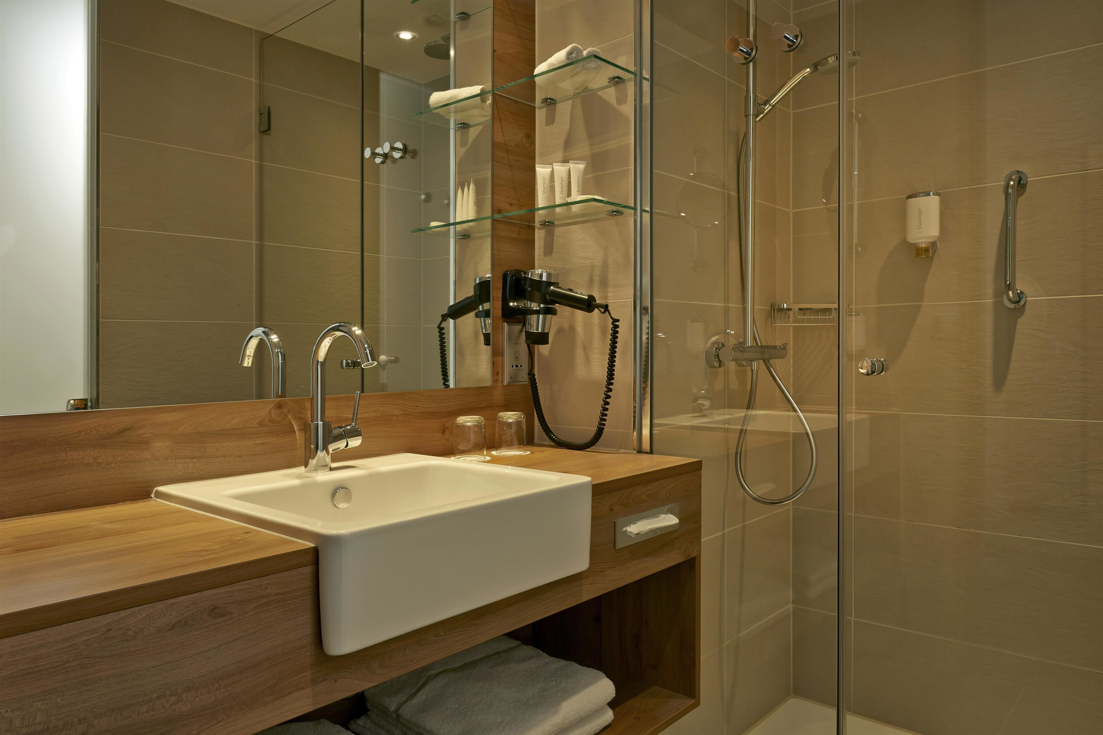 A modern bathroom with a wooden vanity, a large mirror, a glass shower enclosure, and a handheld showerhead.