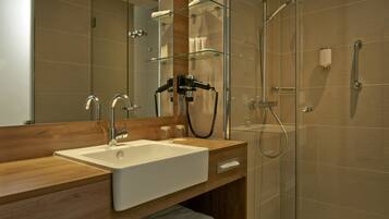 A modern bathroom with a wooden vanity, a large mirror, a glass shower enclosure, and a handheld showerhead.
