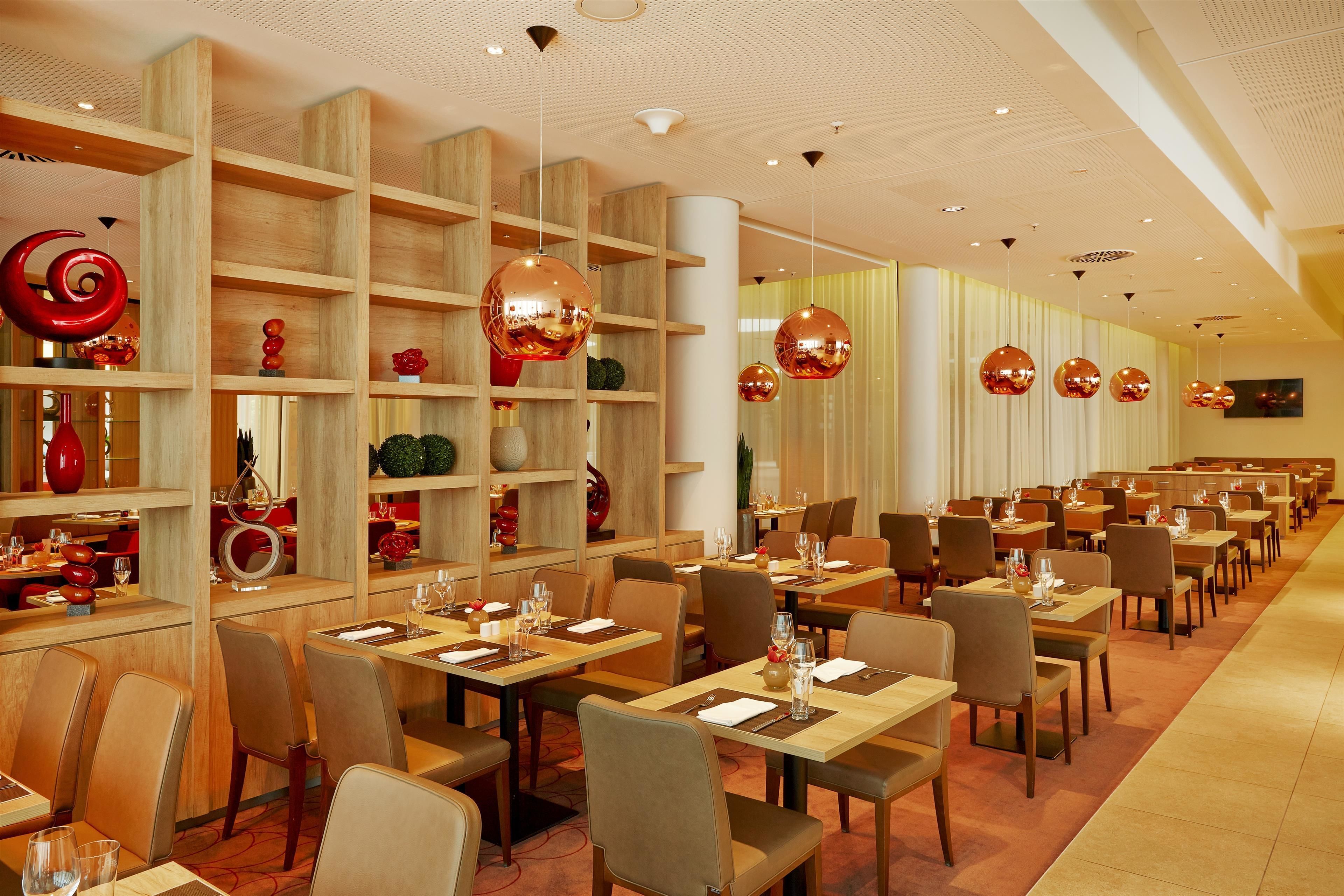 A spacious restaurant with multiple dining tables and chairs, wooden shelves with decorative items, and hanging spherical light fixtures.