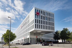 A modern H4 Hotel building with a prominent logo, a flat facade, and a parking sign indicating a direction. - H4 Hotel München Messe (Munich)