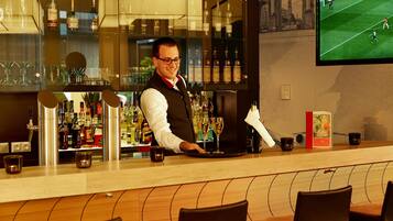 A bar area with a bartender, shelves of liquor bottles, glasses, and a television displaying a soccer game.