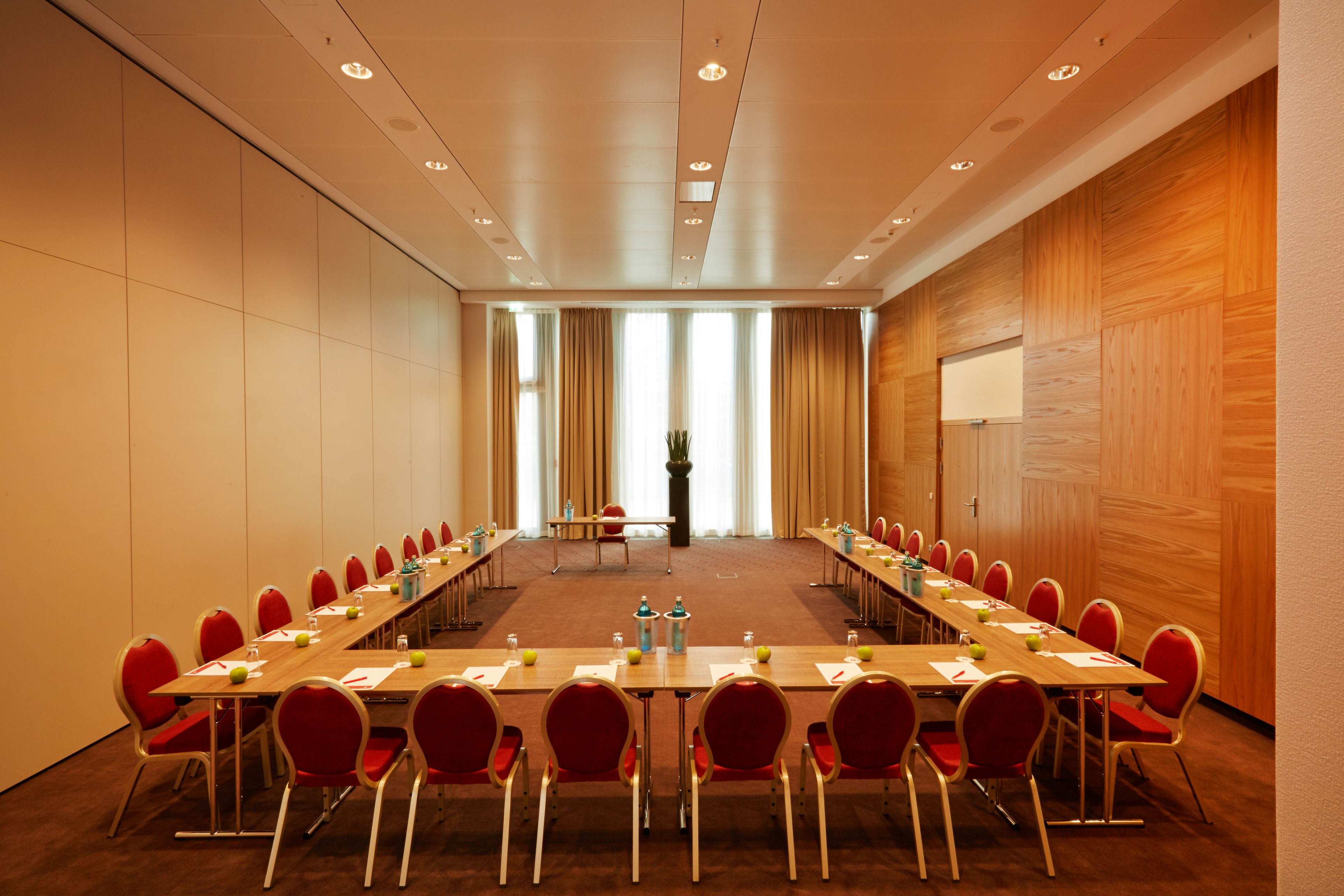 A conference room with a long table, red chairs, and a projector screen on the wall.