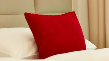 A bed with a red pillow and a white pillow, a beige headboard, and a light switch on the headboard.