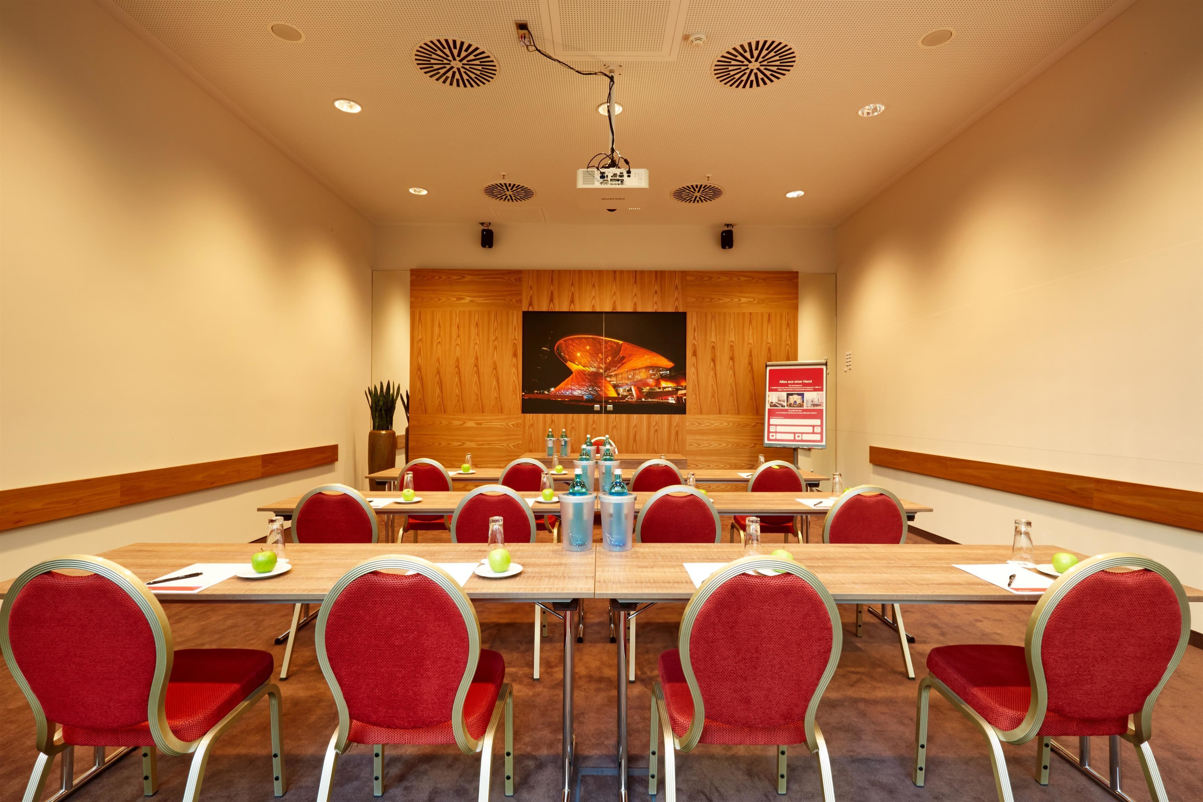 A conference room with a long table, red chairs, a projector, and a large painting on the wall.