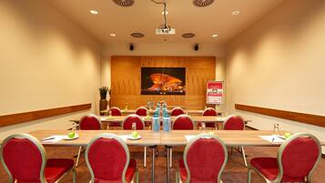A conference room with a long table, red chairs, a projector, and a large painting on the wall.