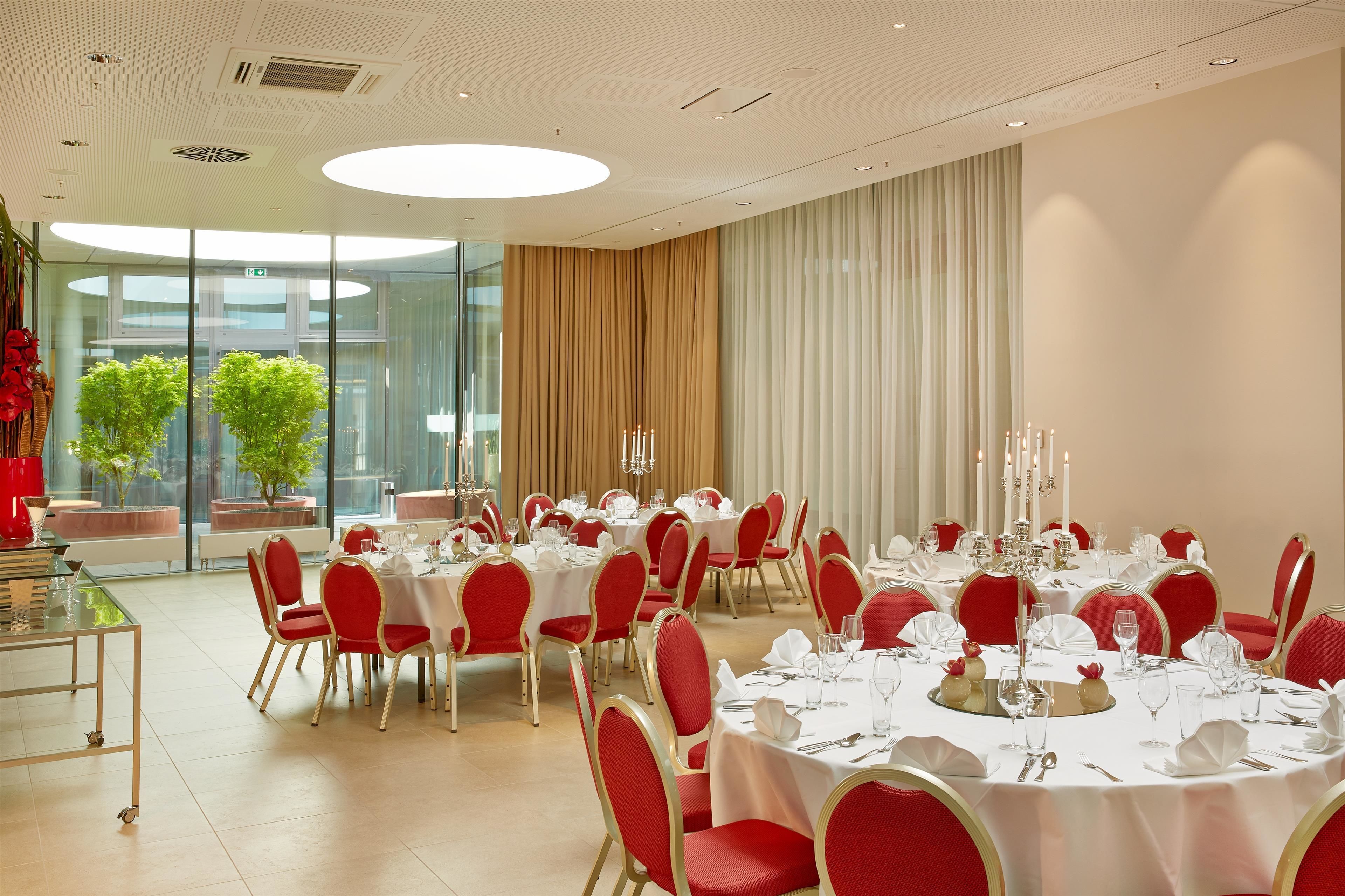 Une salle à manger élégante, avec des tables rondes, des chaises rouges et des nappes blanches.