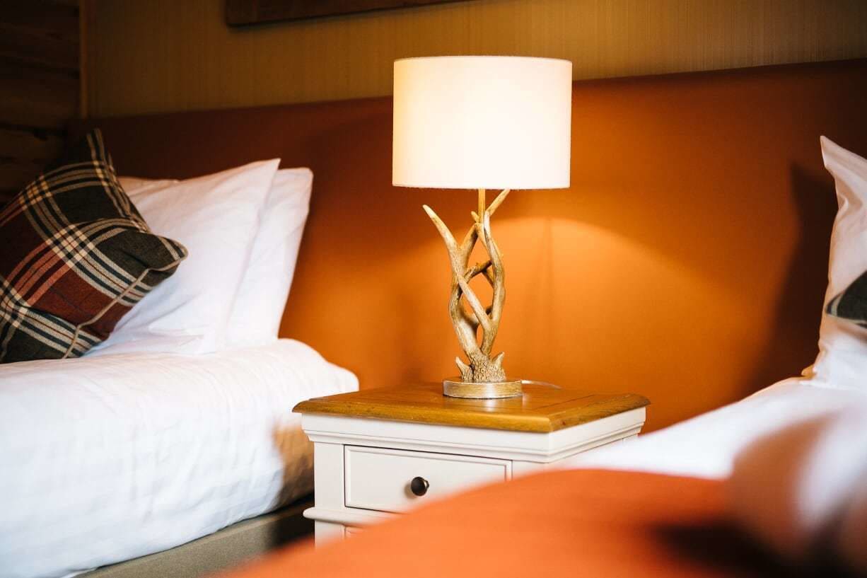 Een hotelkamer met een bed, een nachtkastje met een lamp en een houten hoofdeinde.