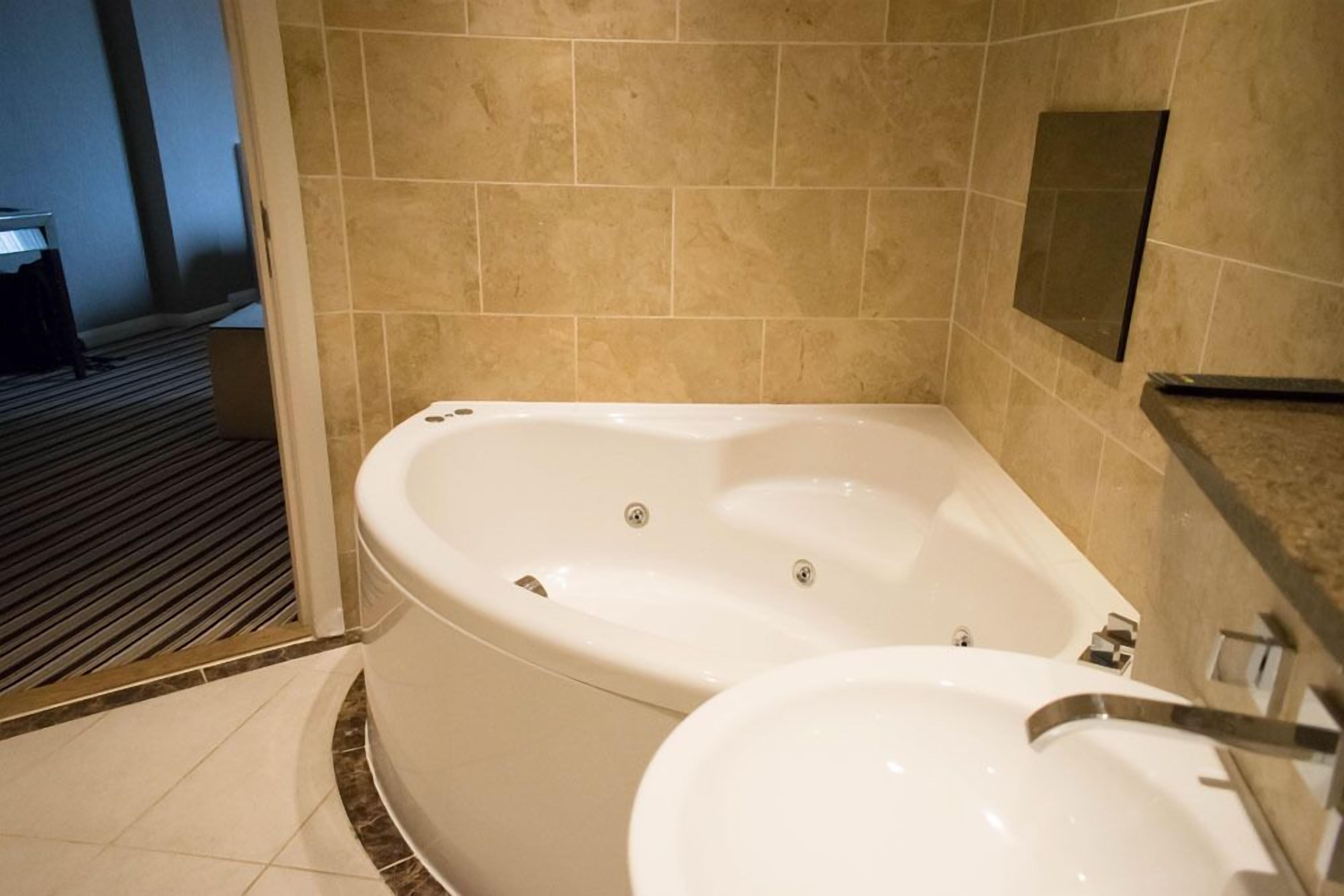 A bathroom with a large bathtub, a sink, and beige tiled walls.