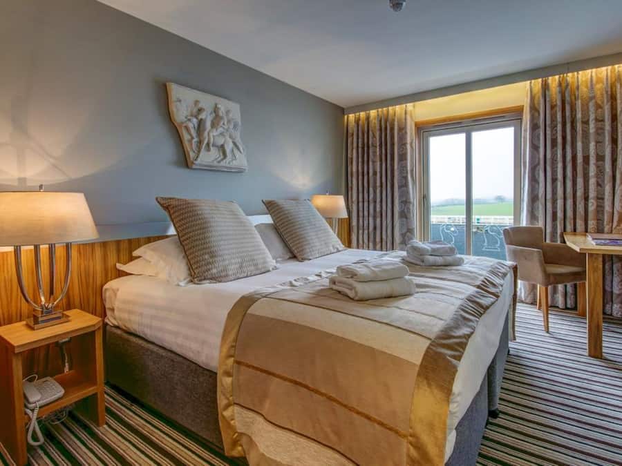 A hotel room with a large bed, two bedside lamps, a desk with a chair, and a view of the outdoors.