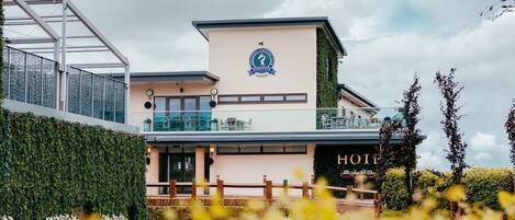 Un hotel moderno con terraza en la azotea, un logotipo en el edificio y un cartel con el nombre del hotel.