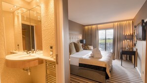 A hotel room with a large bed, a separate bathroom with a double sink, a flat-screen TV, and a view of the outdoors. - Ingliston Country Club Hotel (Bishopton)