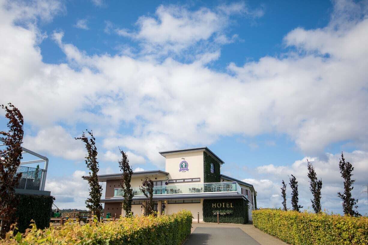 A modern hotel with a prominent 'HOTEL' sign, a glass entrance, and a well-maintained garden area.