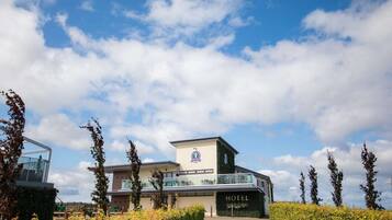 A modern hotel with a prominent 'HOTEL' sign, a glass entrance, and a well-maintained garden area.