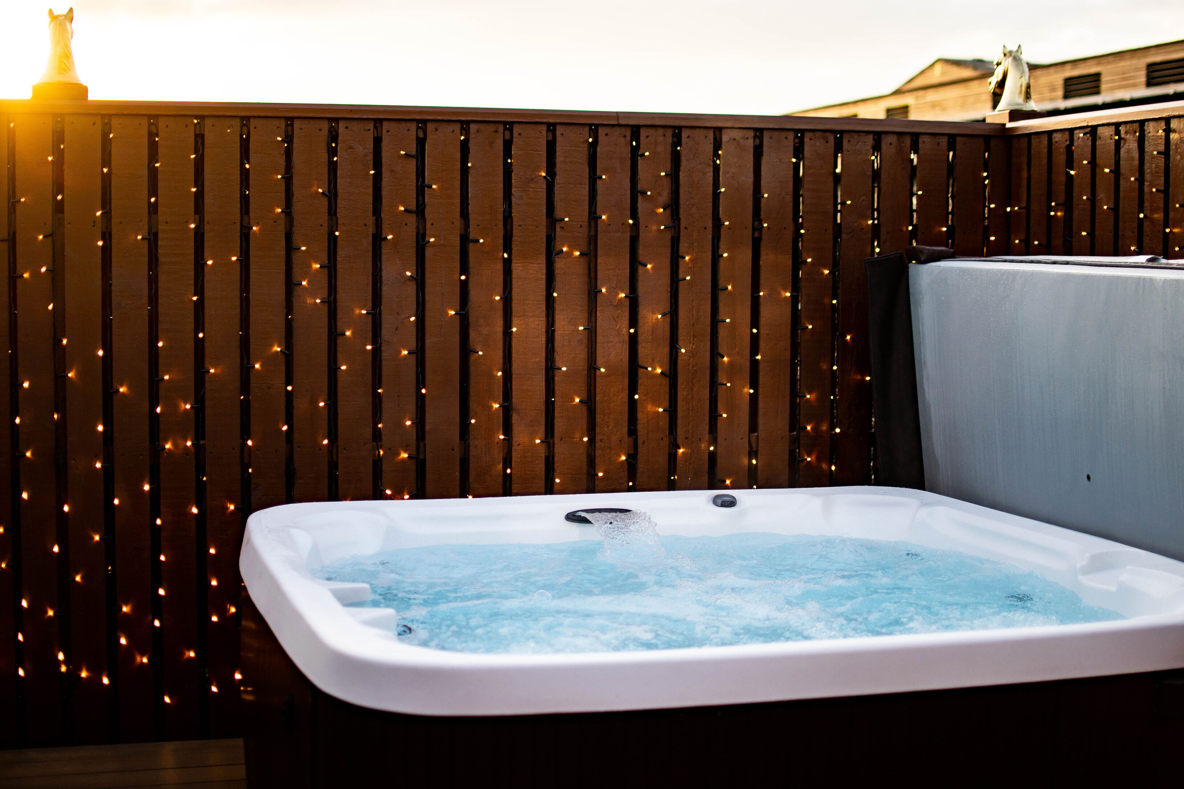 A hot tub with a wooden fence and string lights in the background.