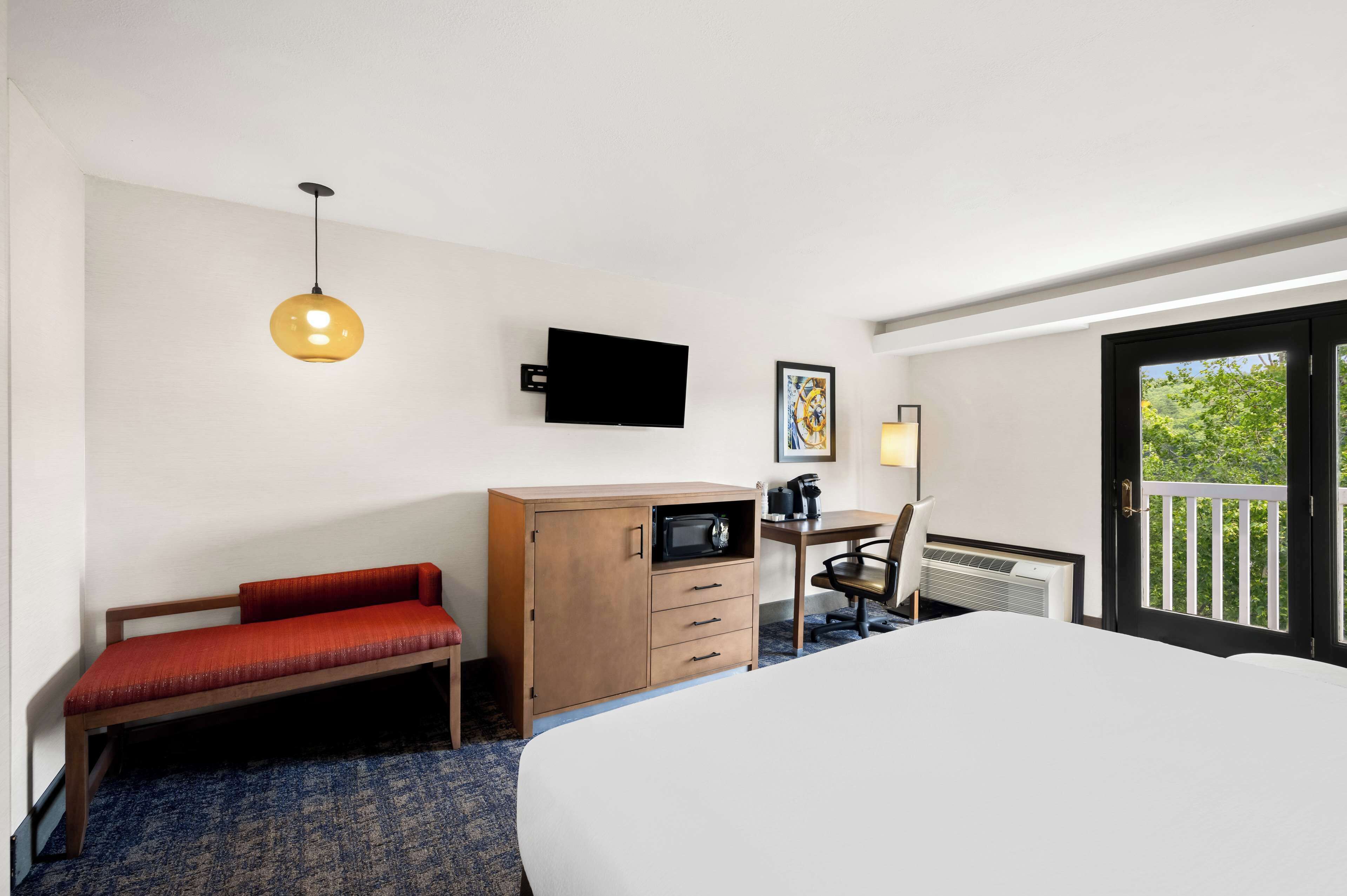 A hotel room with a bed, a desk with a chair, a television, a microwave, and a sliding door to a balcony.