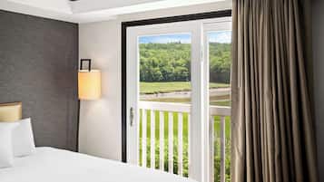 Relax in a serene space with a large bed, bedside table, and sliding door leading to a lush green view.