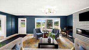A living room with two armchairs, a coffee table, and a TV. There is a door leading outside, a window with a view, and a patterned wall. - Best Western Freeport Inn (Freeport)