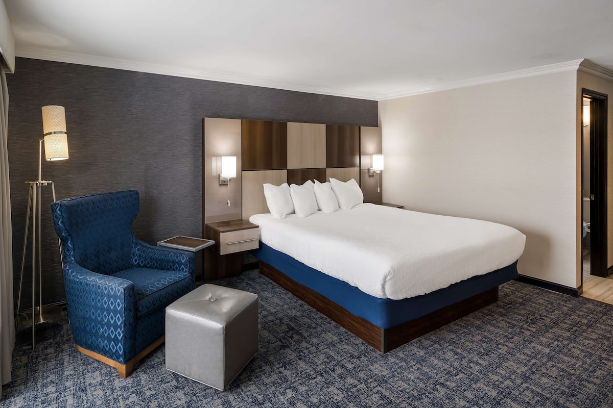 A hotel room with a large bed, a blue armchair, a small table, and a bedside lamp.