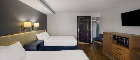 Una habitación de hotel con dos camas, un mueble de madera con microondas, un televisor de pantalla plana y una puerta que da a un baño.