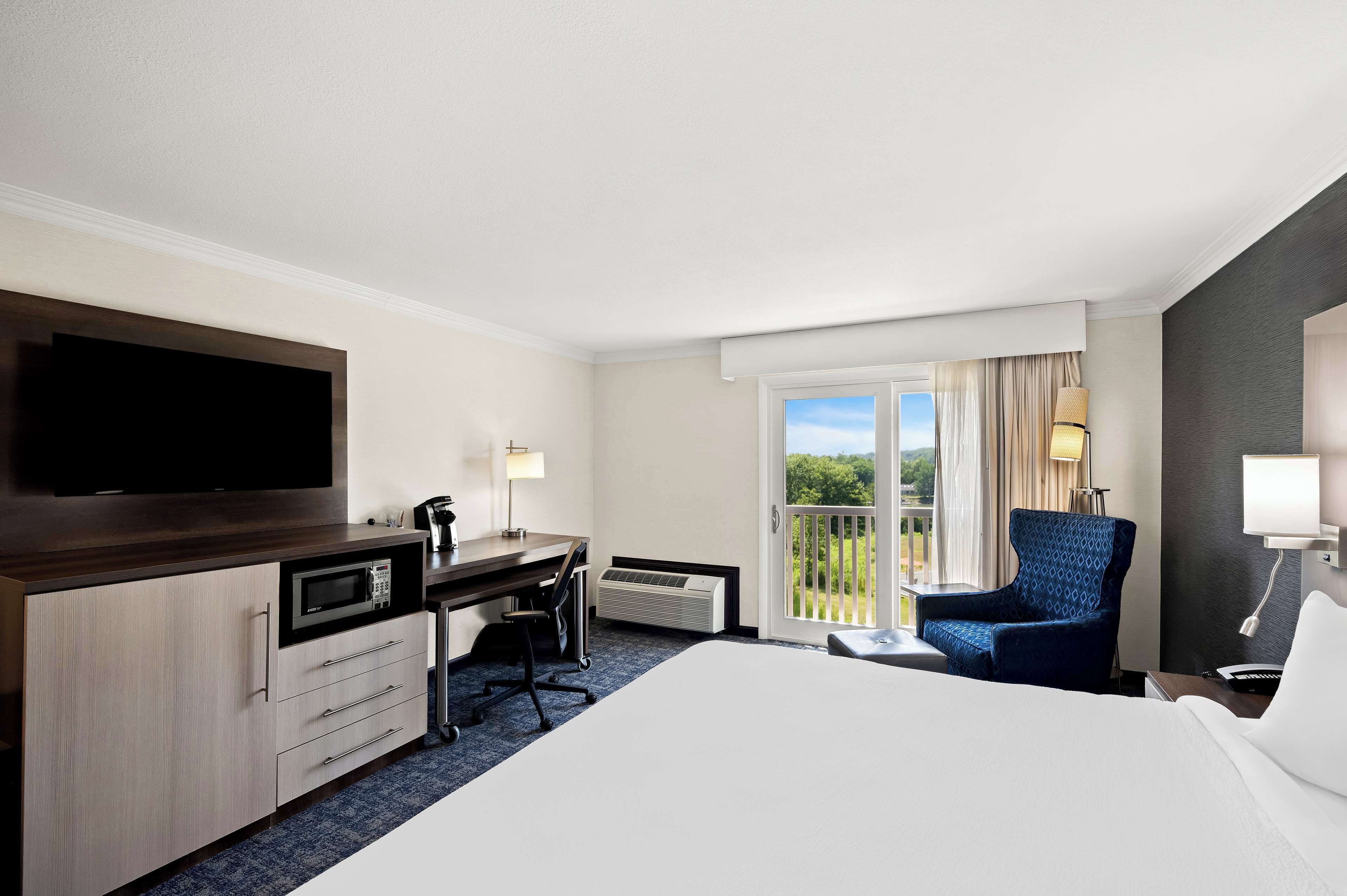 A hotel room with a bed, desk, chair, television, and a balcony with a view.
