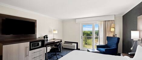 A hotel room with a bed, desk, chair, television, and a balcony with a view.