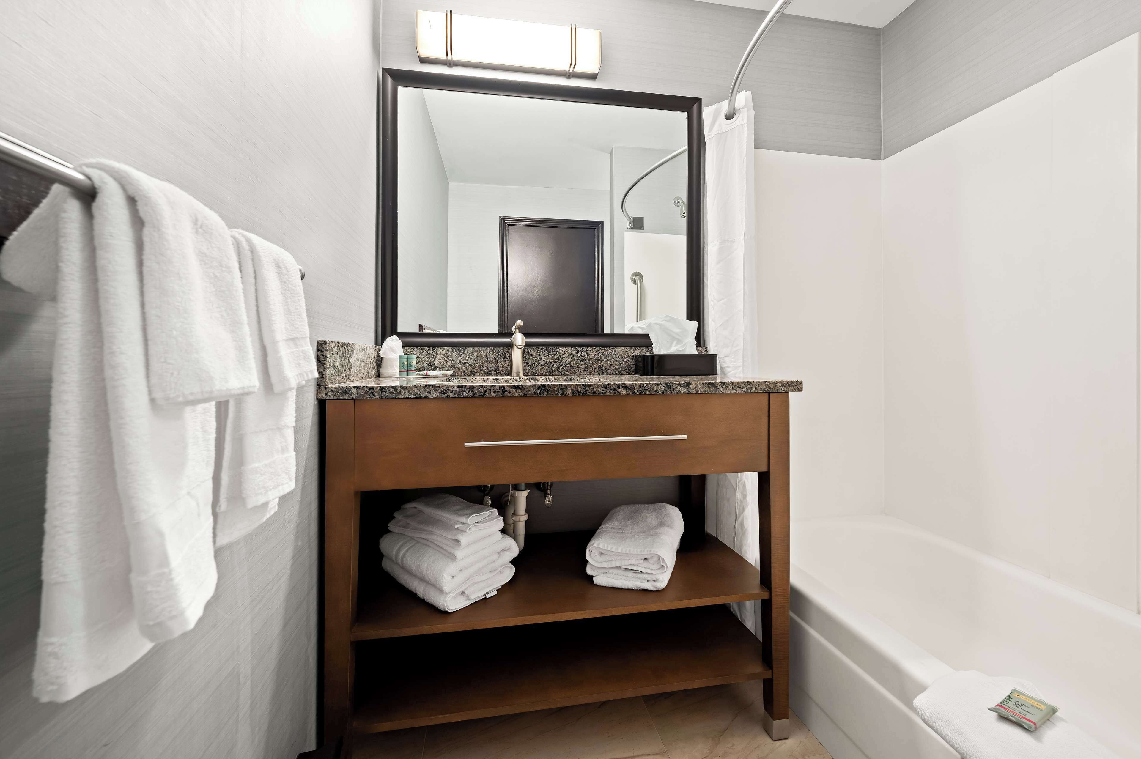 A bathroom with a wooden vanity, a sink, and a mirror. There are towels on the wall and shelves under the vanity.