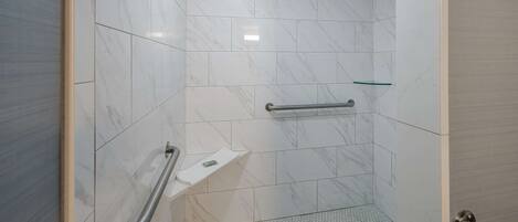 A bathroom with white marble tiles, a handrail, and a small shelf.