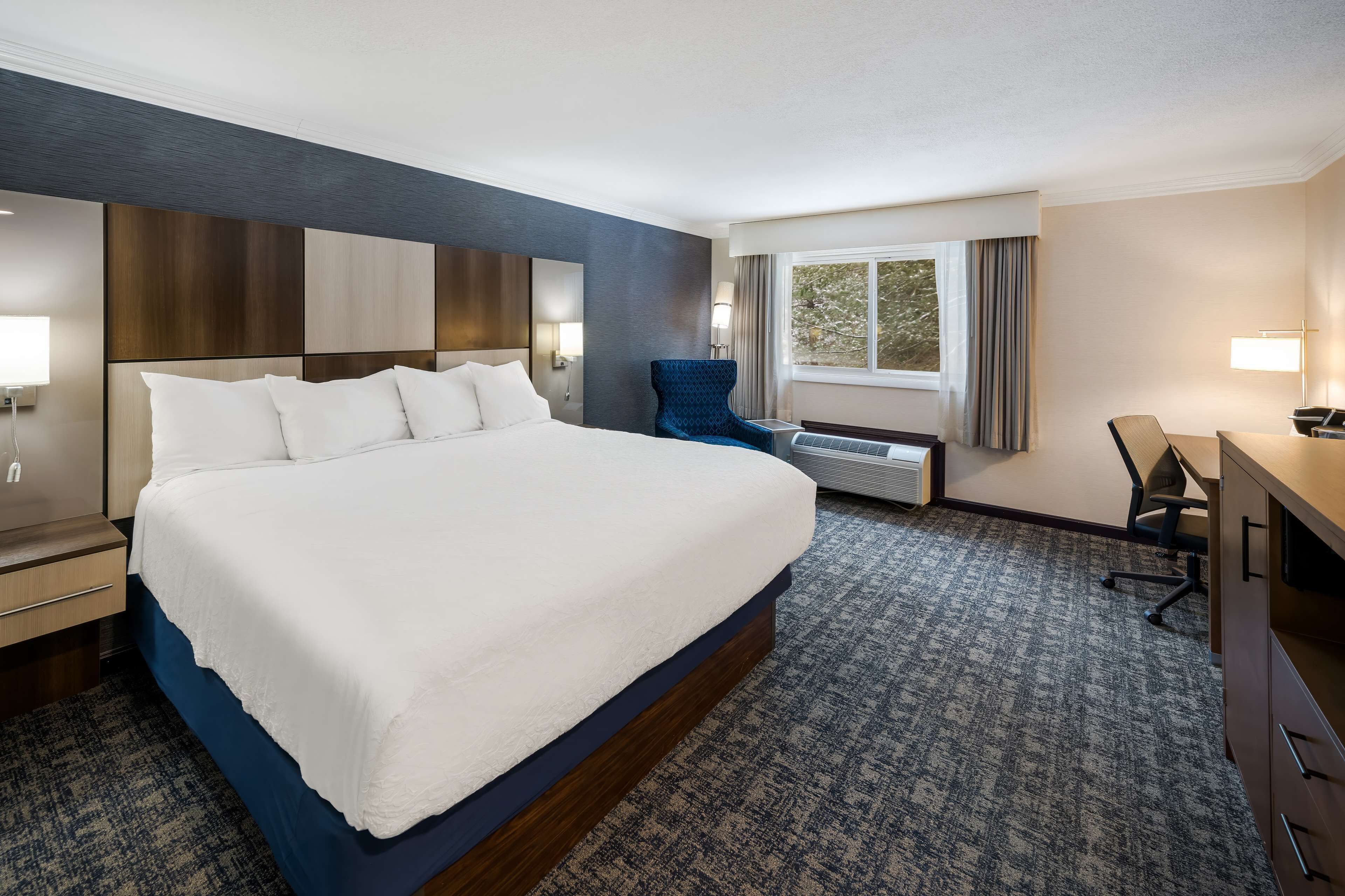 A hotel room with a large bed, a desk, a chair, and a window with curtains.