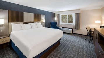 A hotel room with a large bed, a desk, a chair, and a window with curtains.