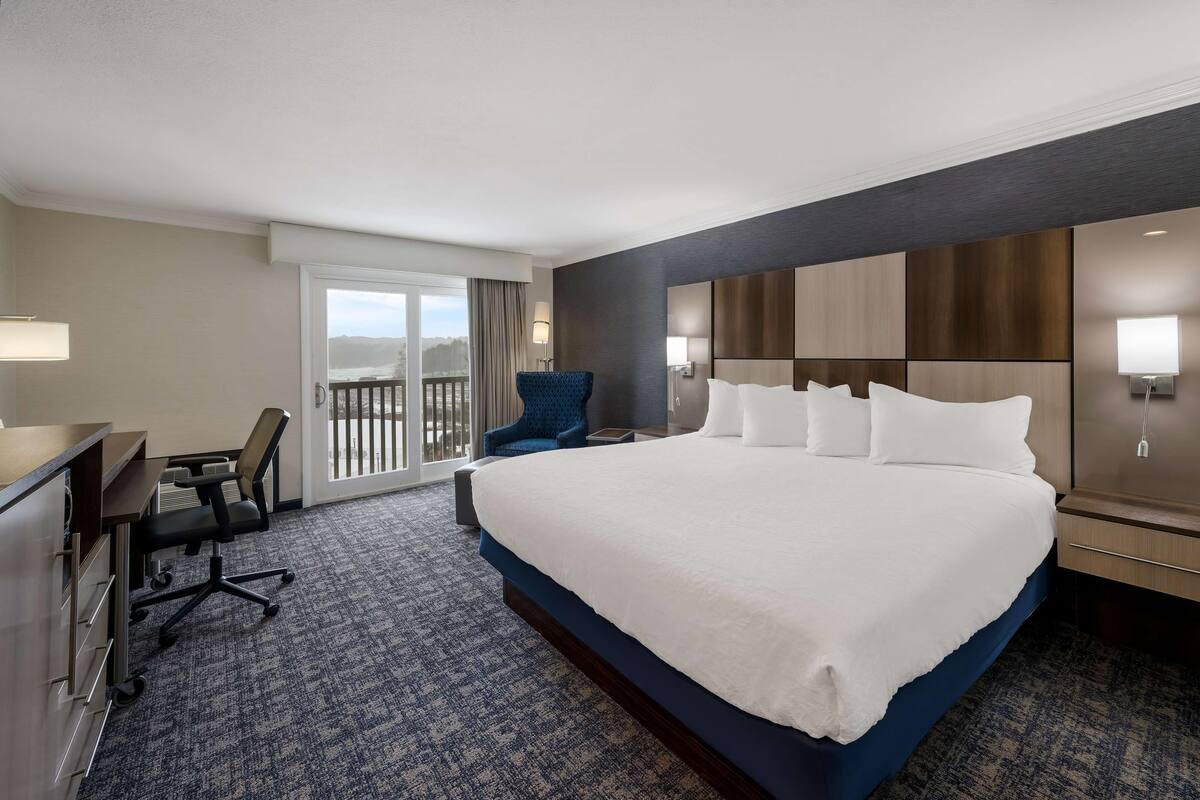A hotel room with a large bed, a desk with a chair, a balcony with a view, and a modern design.