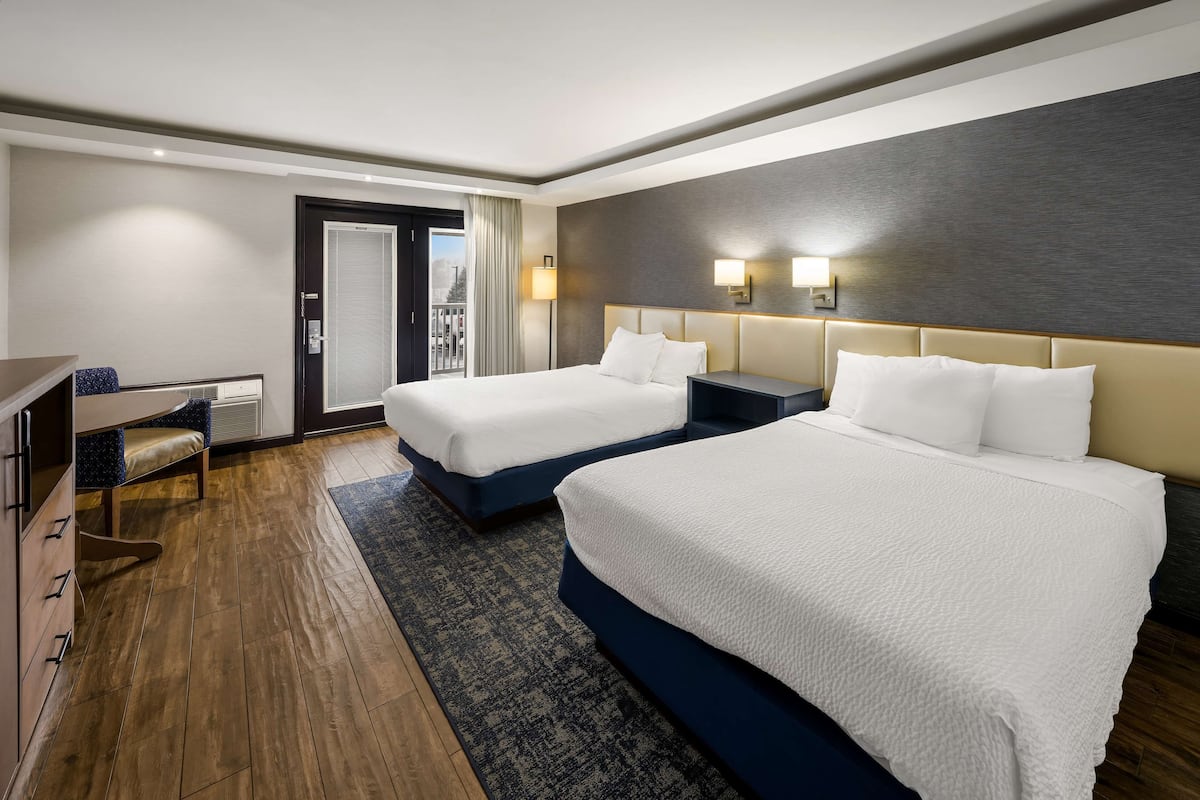 A hotel room with two beds, a desk, and a view of the outdoors.