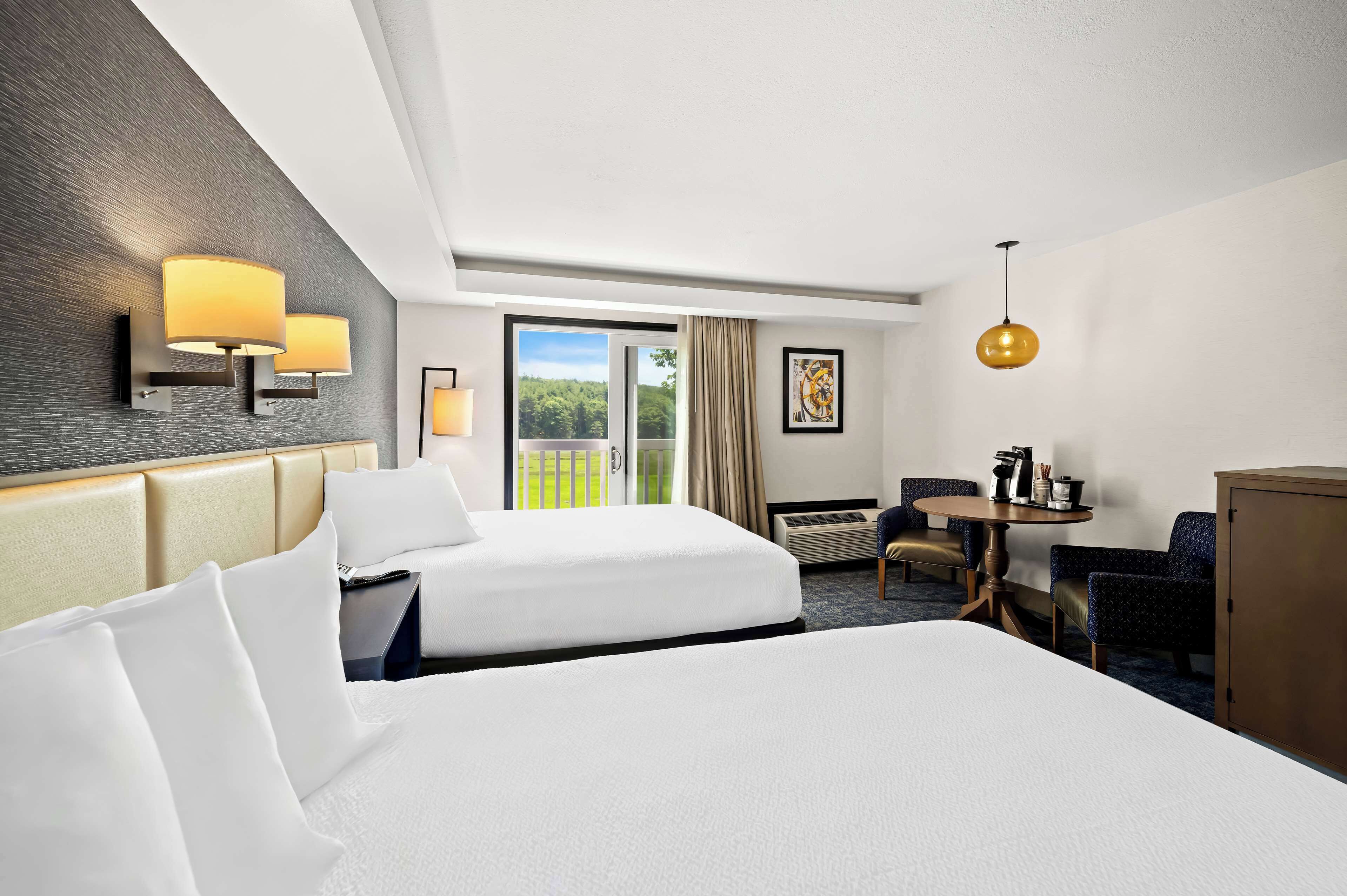 Ein Hotelzimmer mit zwei Betten, einem Schreibtisch, einem Stuhl, einem Tisch und Blick ins Freie.
