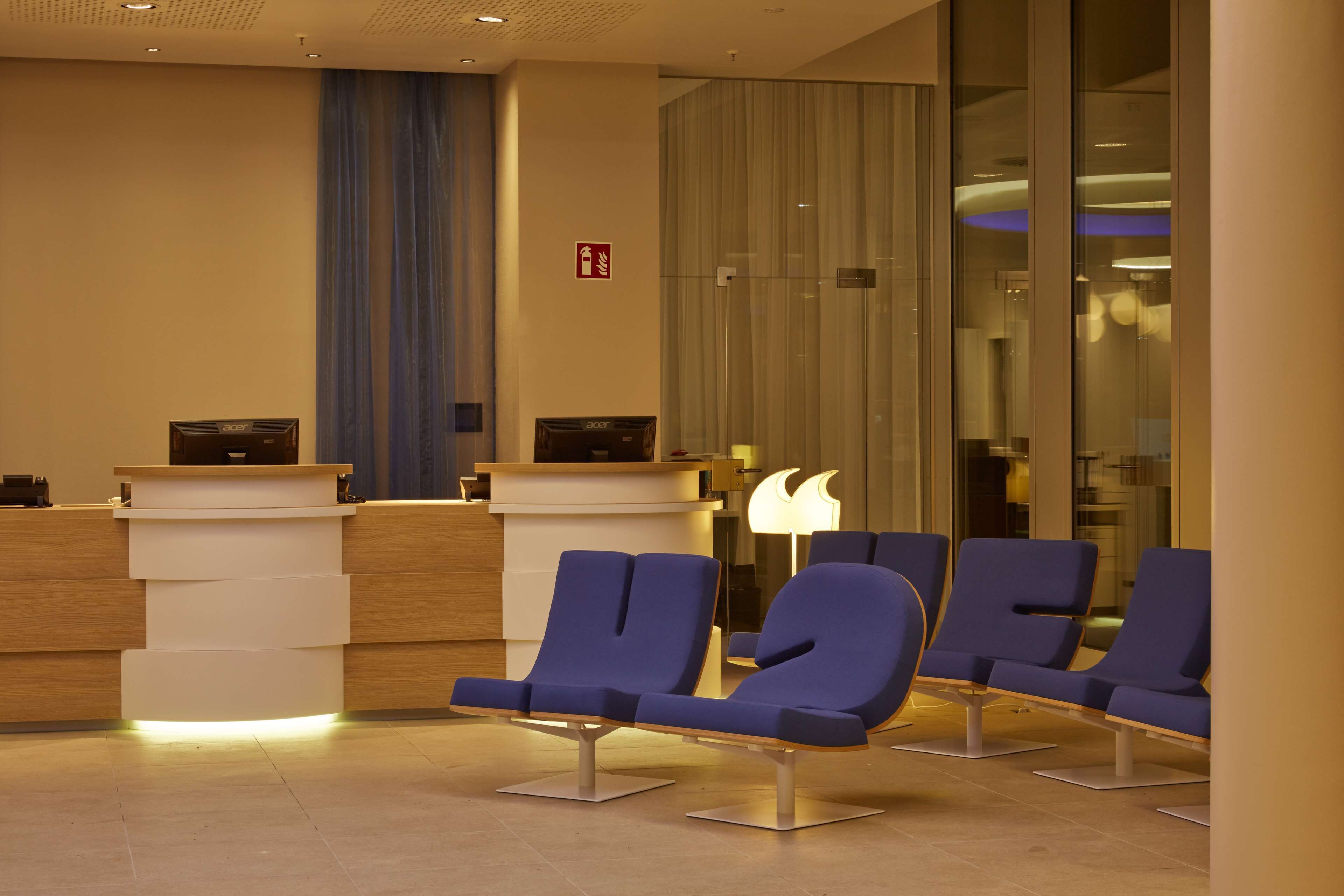 Un espace d’accueil au design moderne, comprenant un comptoir de réception, des sièges bleus et une cloison en verre.