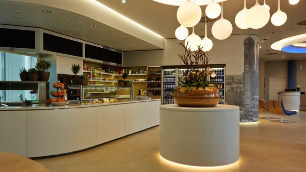 A modern hotel lobby with a central reception desk, a large decorative planter, and a seating area with chairs. - H2 Hotel München Messe (Munich)