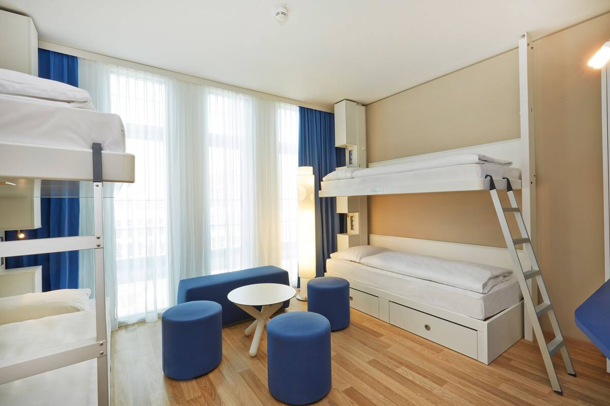 Habitación de hotel con literas, una mesita redonda y otomanas azules.