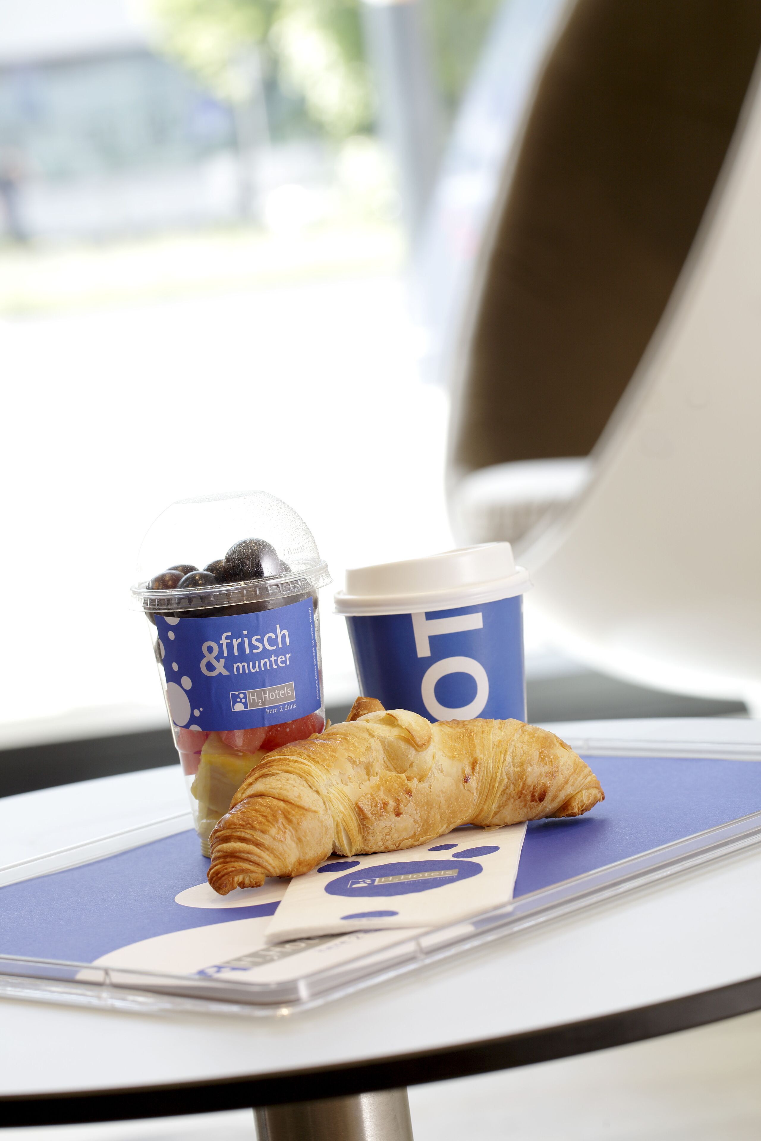 Un croissant y una taza de café sobre una mesa con diseño azul y blanco.