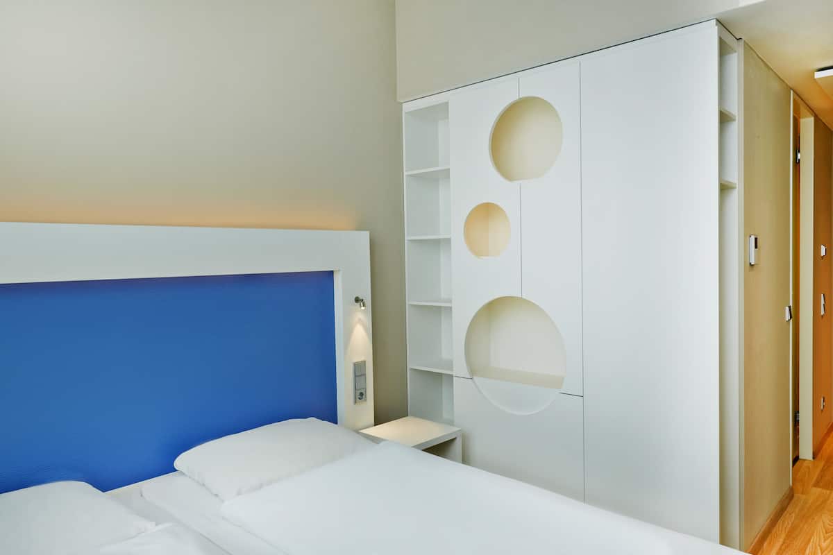 Una habitación de hotel moderna con una cama grande, un armario blanco con detalles circulares y una mesita de noche pequeña.