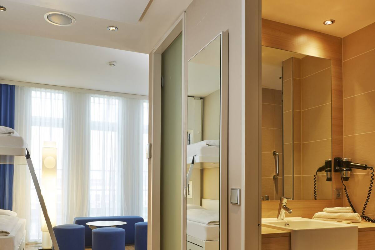 Una habitación de hotel moderna con suelo de madera, sofá, espejo, lavabo y secador de pelo.