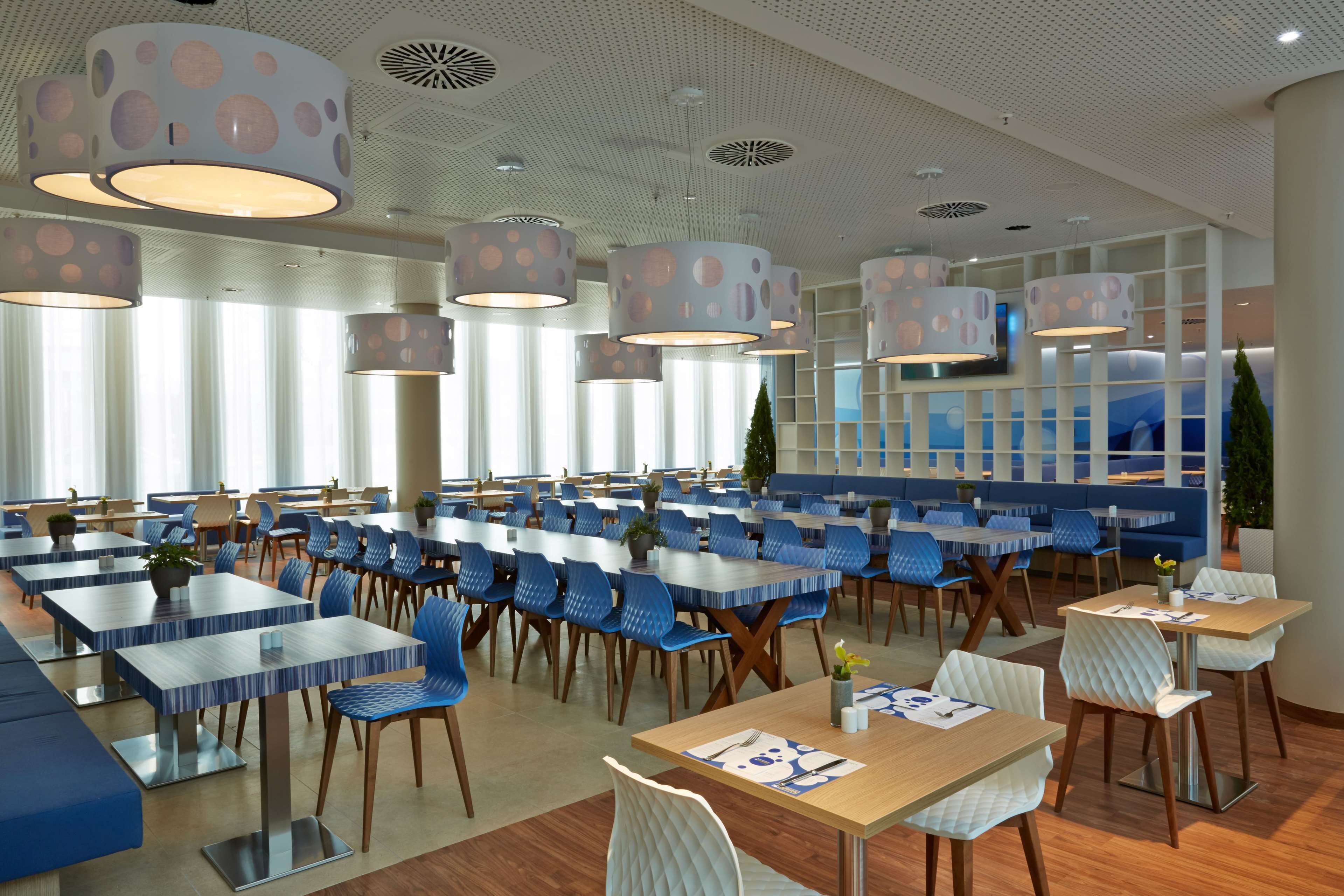 Un espace repas moderne doté de plusieurs tables et chaises, avec un plafond orné de motifs circulaires et un éclairage encastré.