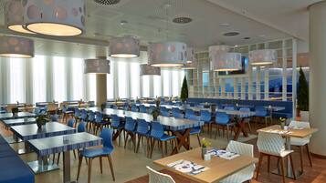 Un espace repas moderne doté de plusieurs tables et chaises, avec un plafond orné de motifs circulaires et un éclairage encastré.