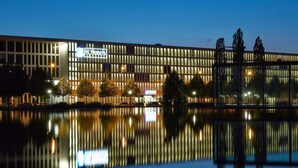 A modern hotel with a reflective pool in front, featuring a prominent 'H Hotels' sign. - H2 Hotel München Messe (Munich)