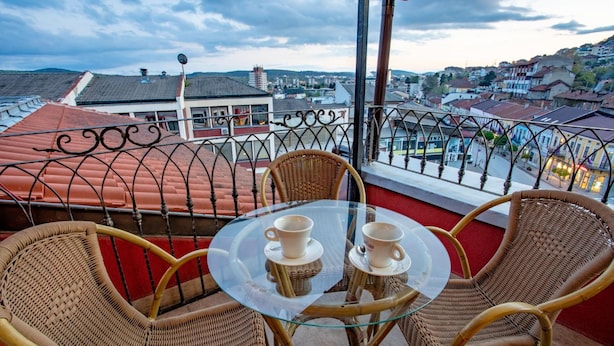 A balcony with wicker chairs and a glass table, overlooking a cityscape with red-roofed buildings. - Real Hotel Veliko Tarnovo (Veliko Tarnovo)