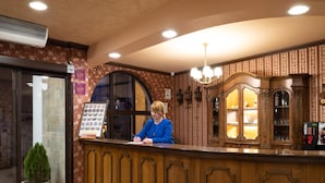 A reception desk with a person seated behind it, a framed menu board, and a decorative wooden cabinet with glass doors. - Real Hotel Veliko Tarnovo (Veliko Tarnovo)