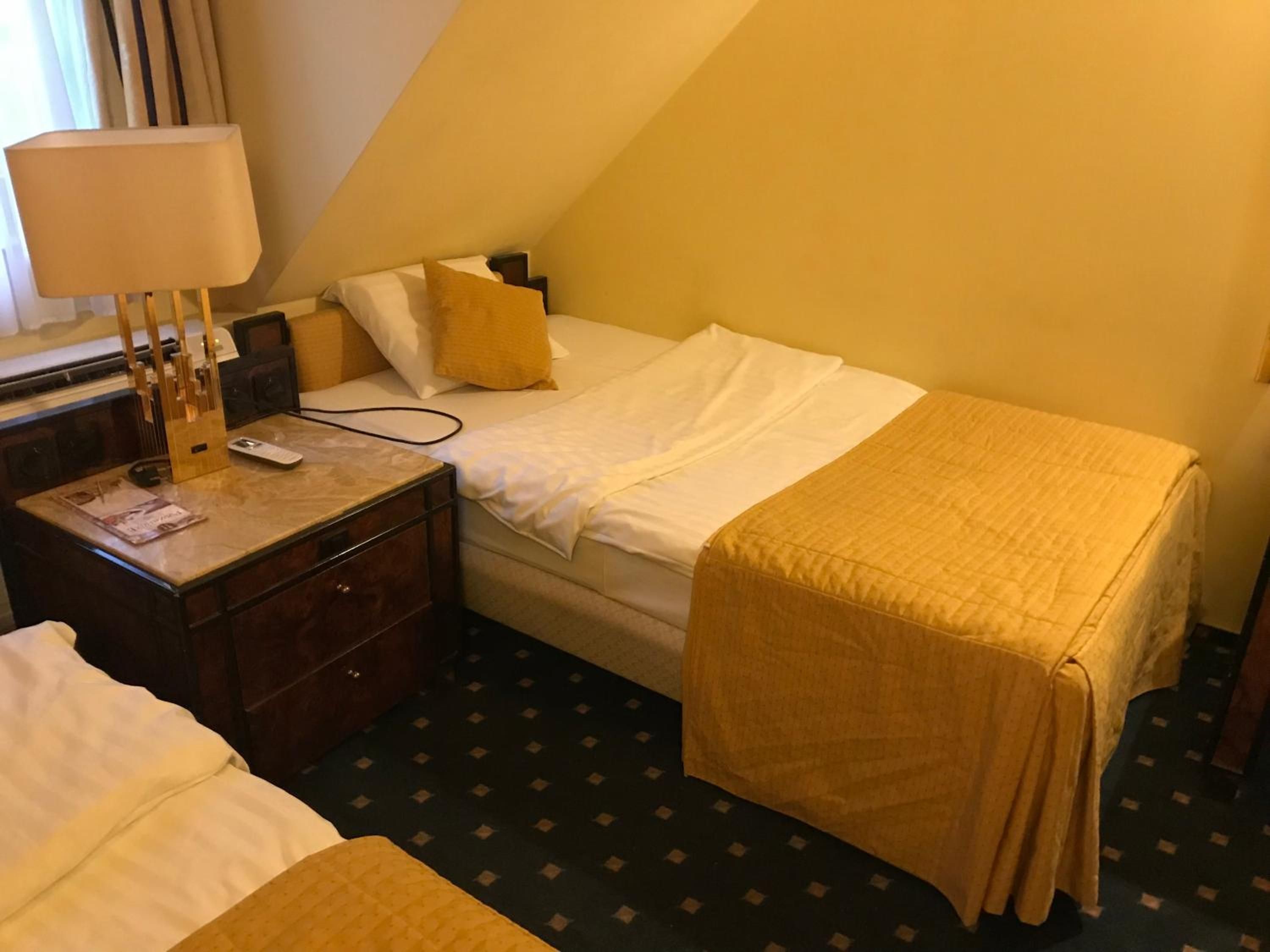 Een hotelkamer met een bed, nachtkastje, lamp en een klein bureau met stoel.