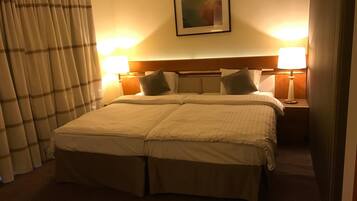 Habitación de hotel con cama doble, dos lámparas de noche, cabecero y un cuadro en la pared.