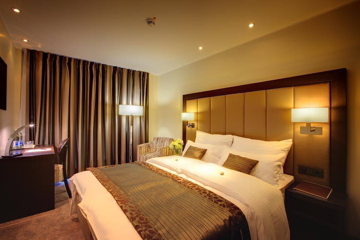 A hotel room with a large bed, bedside lamps, a desk with a lamp, and curtains.