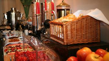 Un buffet proposant une variété de plats, notamment des fruits et des pâtisseries, ainsi qu’un panier en osier rempli de pain.